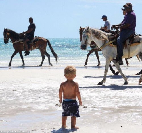 Cậu bé Manilla nhìn những người đàn ông cưỡi ngựa dọc bãi biển trên quần đảo Turks & Caicos.