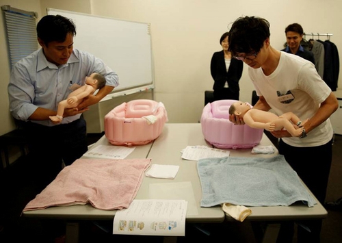 Yuji Inoue (trái), 42 tuổi và Takashi Tayama (phải), 35 tuổi đang thực hành kĩ năng chăm sóc em bé tại lớp học. ẢNH: REUTERS