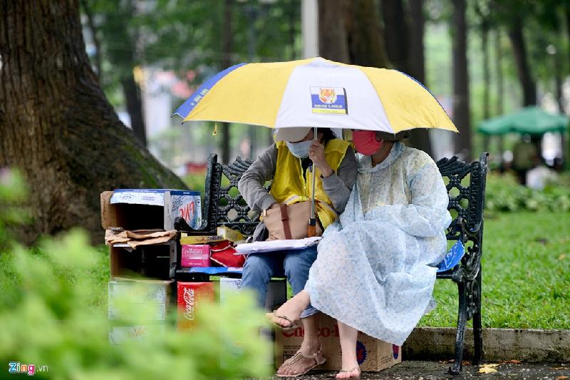 Hai người phụ nữ vừa mang áo mưa, ô vừa chờ khách mua nước trong công viên 30-4, quận 1.