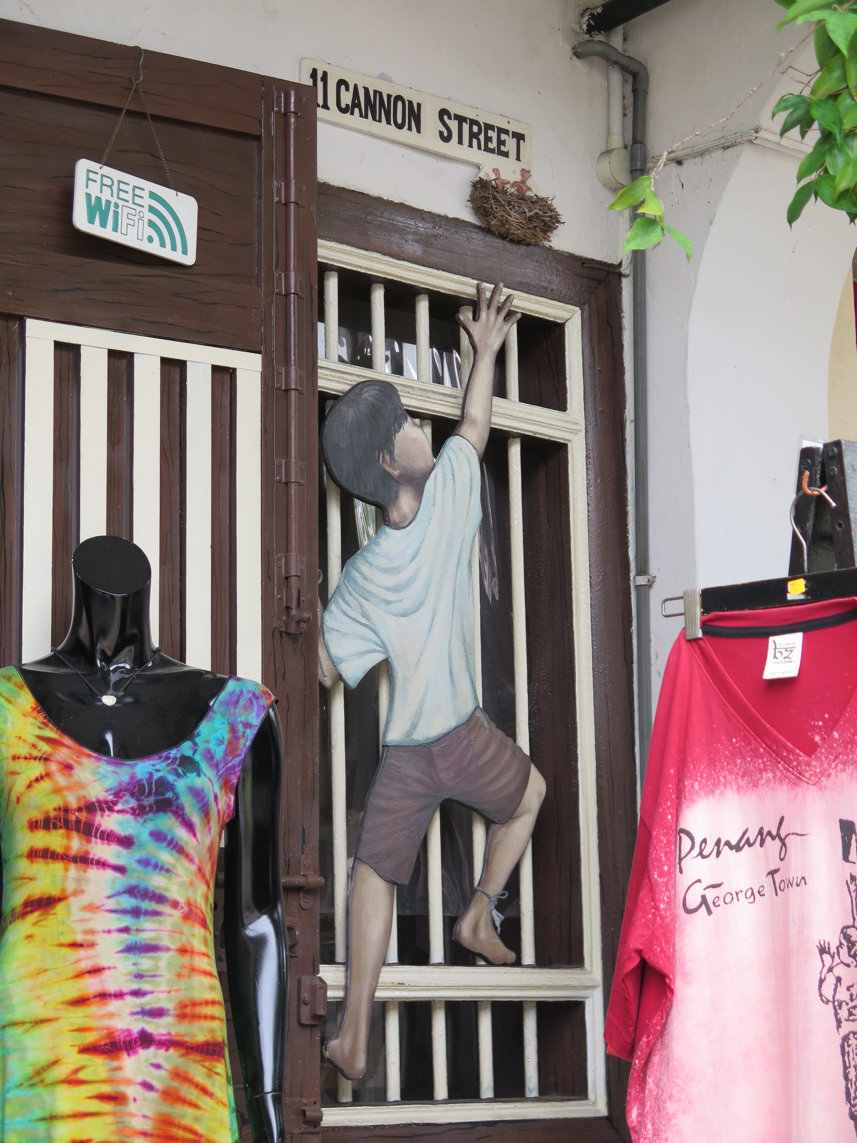 Một chú bé đang trèo cửa sổ với tay tới tổ chim trước cửa một shop thời trang
