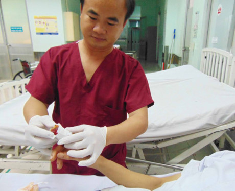 Bác sĩ Vũ Minh Đức kiểm tra ngón tay sắp đứt lìa của anh H. Ảnh: TRẦN NGỌC