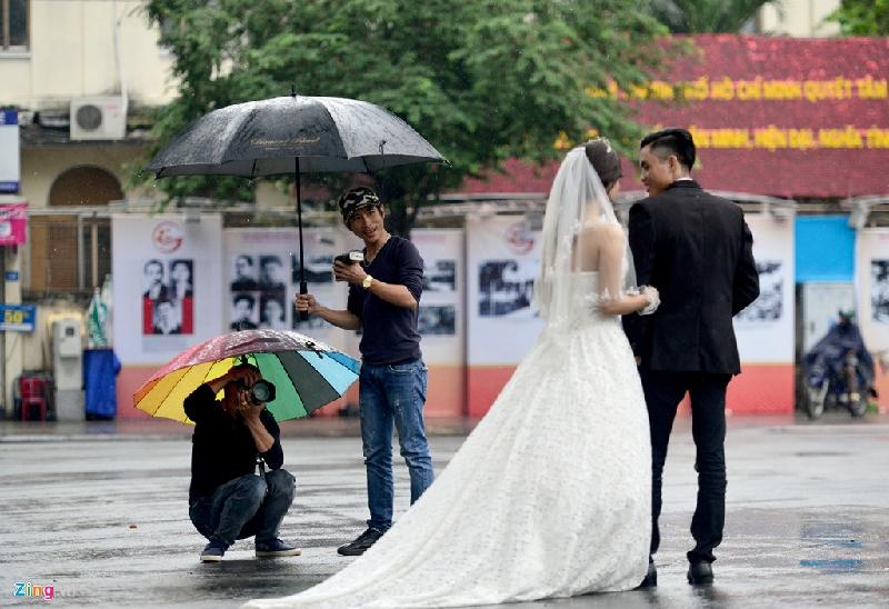 Cặp cô dâu-chú rể cùng thợ chụp ảnh say sưa tạo dáng, chụp hình giữa trời mưa trước nhà thờ Đức Bà.