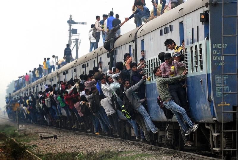 Các hành khách Ấn Độ không có chỗ ngồi bên trong phải bám vào cạnh chuyến tàu khởi hành từ một nhà ga ngoại ô New Delhi.