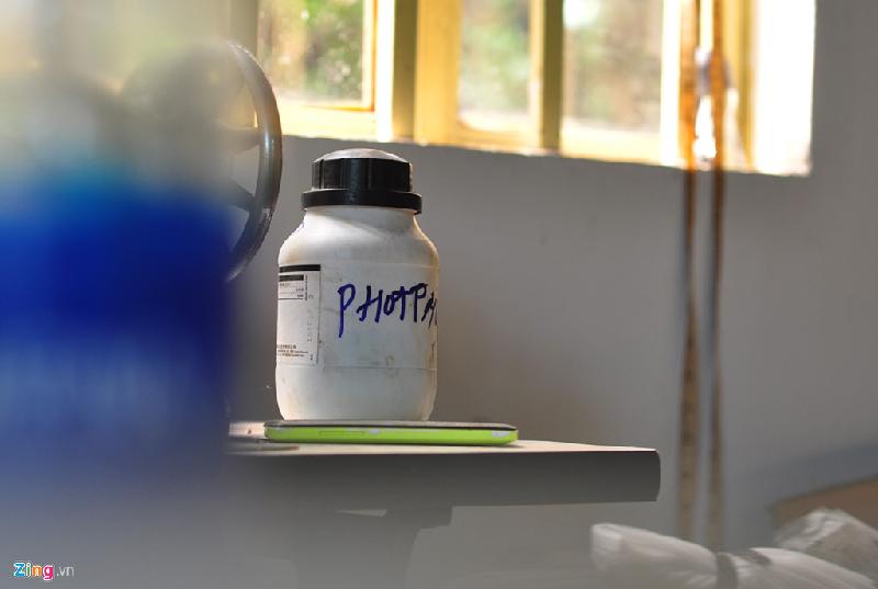Một vỏ chai chứa chất hóa học cùng chiếc điện thoại hỏng được để trên bàn máy may trong căn nhà. 