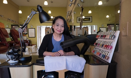 Bà Lan Anh Truong tại bàn làm móng có gắn ống hút mùi từ các sản phẩm làm đẹp tại tiệm nail của mình ở Alameda